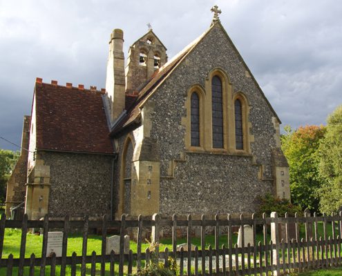 St Johns church in Ashley Green, in strong afternoon sunlight, some grey cloud, and trees turning colour for autumn