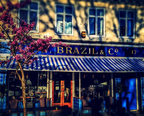 Brazils exterior - blue and gold signage, striped awning and cherry blossom tree in the foreground