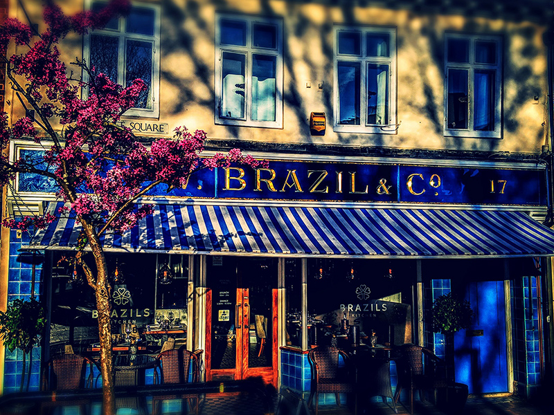 Brazils exterior - blue and gold signage, striped awning and cherry blossom tree in the foreground