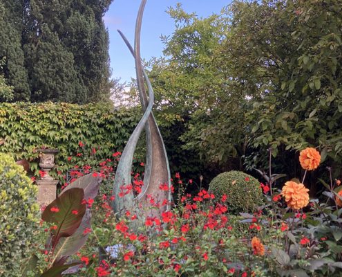 Sculpture in Chehies Manor gardens and orange and red flowers, and hedge