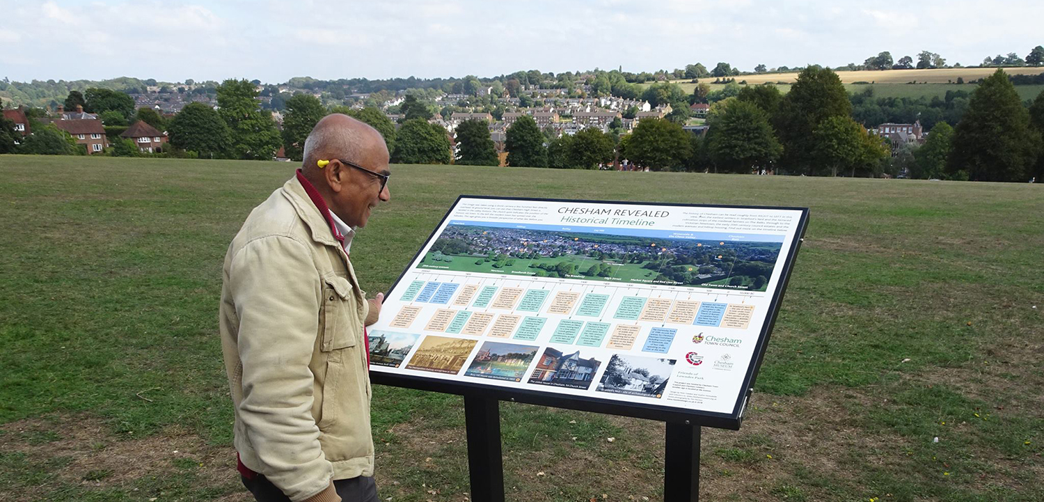 Mature man looking at the historical timeline board at the top of Lowndes Park, with view over Chesham town.
