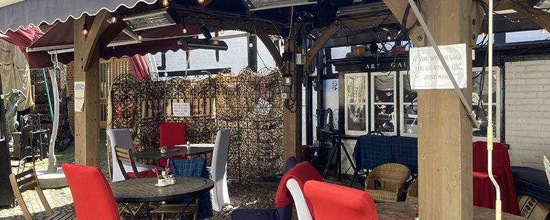 Outdoor seating under cover outside The Drawingroom. high backed red chairs, warm lighting