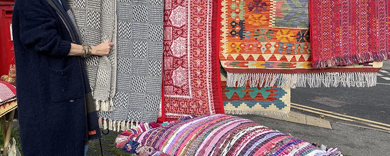 Owner standing with forecourt display of colourful rugs and cushions
