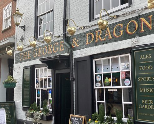 Outside ofThe george and Dragon pub with signage explaining its hostory dating back to the 16th century. The brick parapet facade and ornate bracketry were added in 1715.