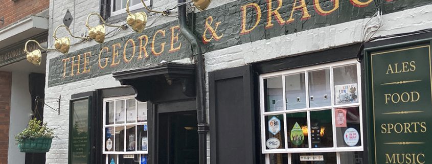 Outside ofThe george and Dragon pub with signage explaining its hostory dating back to the 16th century. The brick parapet facade and ornate bracketry were added in 1715.