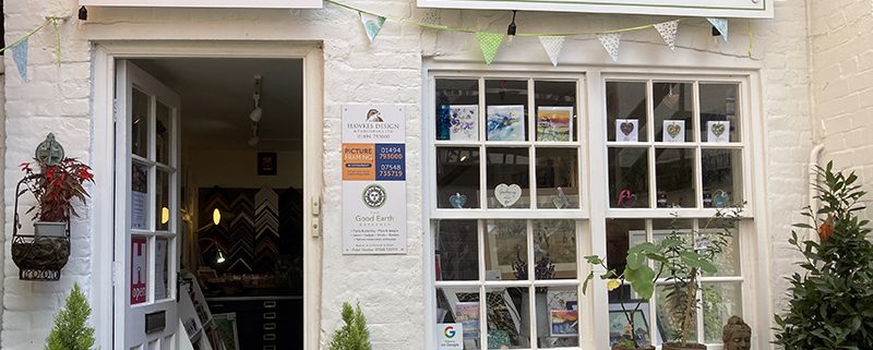 Front of Good Earth gallery with open door and plants and pots and a table outside