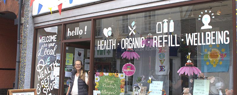 Healthright manager in doorway of shop, and with window front displaying health products