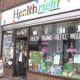Healthright manager in doorway of shop, and with window front displaying health products
