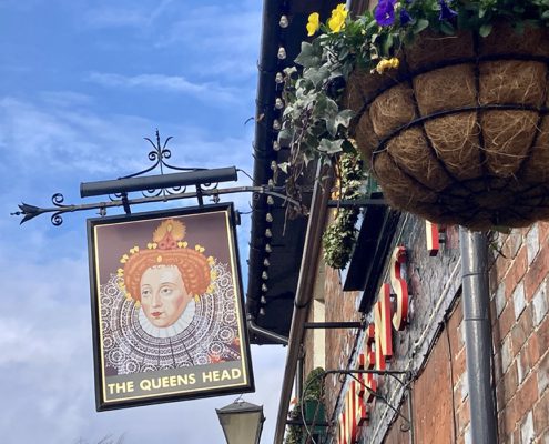 Pub sign depicting Queen Elizabeth the first, flowering hanging basket in the foreground