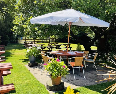 White Hart garden on a sunny day pub benches, round table with parasol, lawn and trees
