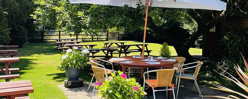 White Hart garden on a sunny day pub benches, round table with parasol, lawn and trees