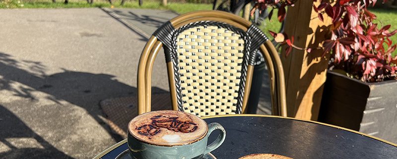 Two cappuccinos with a cocoa powder decoration of cycles with view of bikes and countryside behind