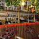 Photo of bar in Lebanese village Milddle Eastern restaauant, whith shelves of bottles, ethnic fabric hangings in front of the bar in warm lighting, and foliage decorating the bar above