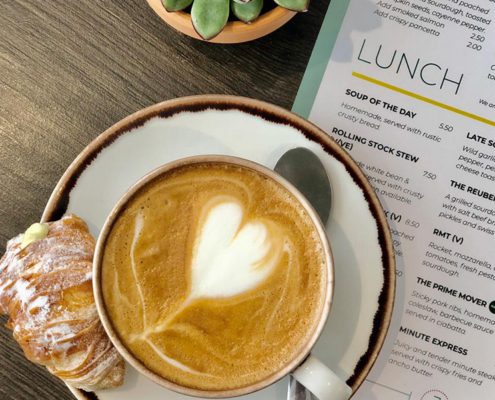 Cappuccino with heart in the froth, and pastry, with a menu underneath on wooden table