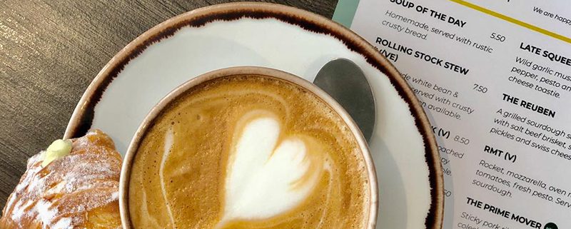 Cappuccino with heart in the froth, and pastry, with a menu underneath on wooden table