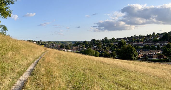 View of dry grassy field and a track with view towards town on sunny day