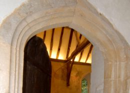 view of the stone archway of old church door with open door looing onto candelit old beams