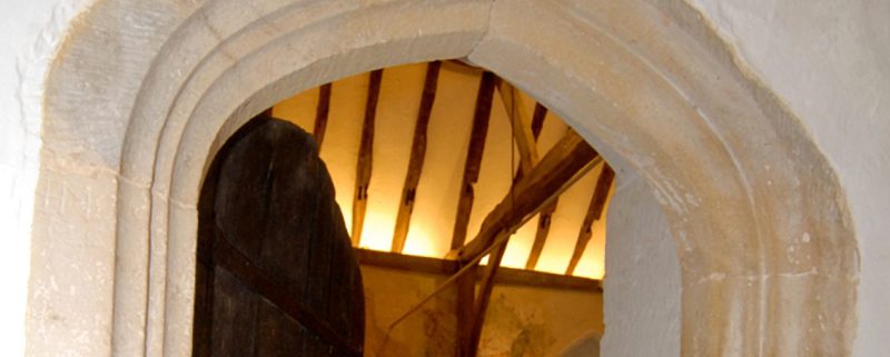 view of the stone archway of old church door with open door looing onto candelit old beams