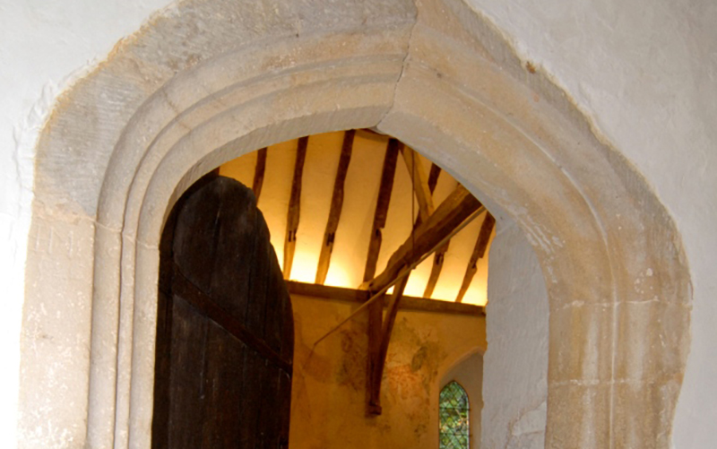 view of the stone archway of old church door with open door looing onto candelit old beams