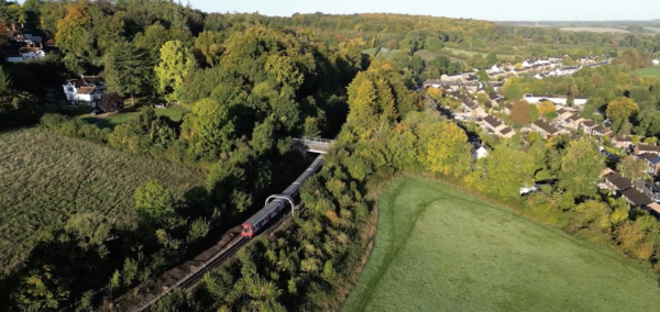 metropolitan line underground train going under a bridge surrounded by woods and fields