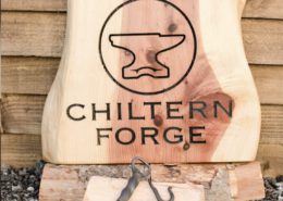 chiltern forgt logo carved into wood, with metalwork hook in the foreground