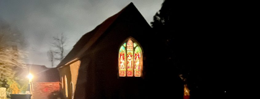 old church it lit up at night, light showing through stained glass windows