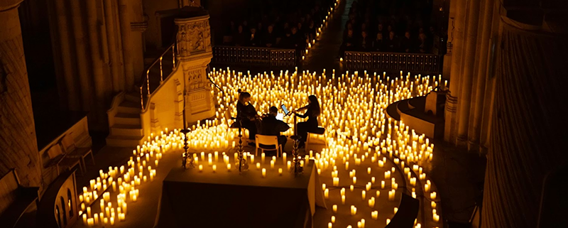 Overhead view of trio of violin players amidst a sea of candlles inside an otherwise unlit theatre