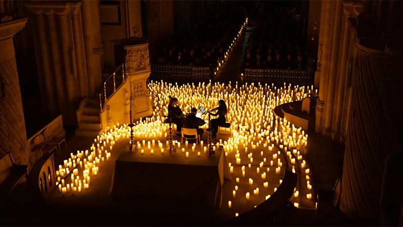 Overhead view of trio of violin players amidst a sea of candlles inside an otherwise unlit theatre
