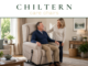 Man sitting in a reclining chair and smiling with person standing beside him miling